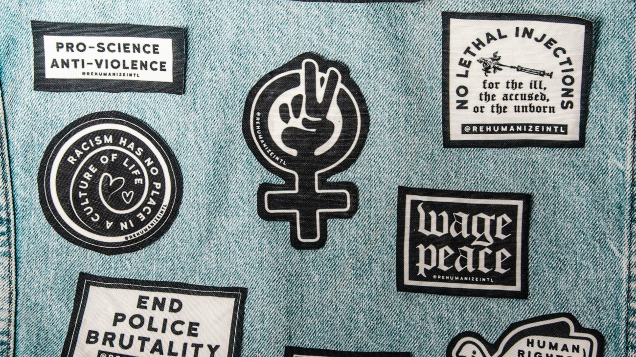 A close-up image of denim fabric featuring multiple black-and-white patches with social justice messages